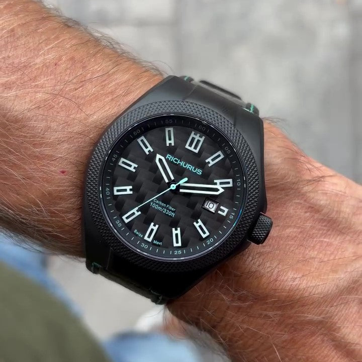 A close-up of a person's wrist wearing a black Rocknroller watch with a black strap and a black dial featuring white Arabic numerals and hands.